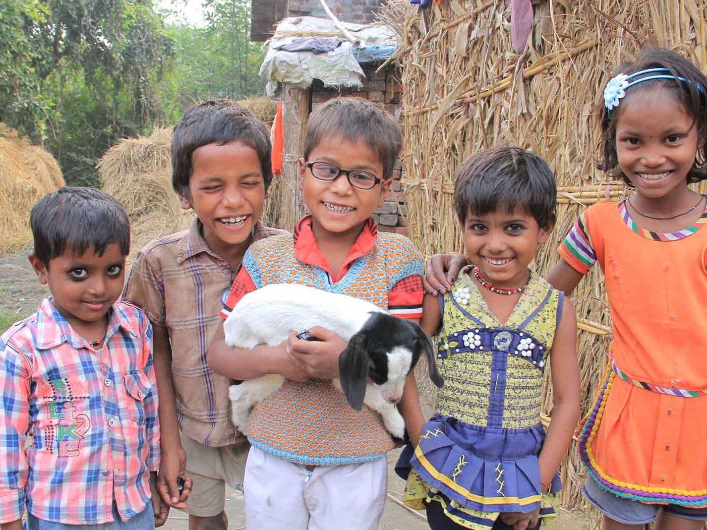 Ein Junge aus Indien hält ein Zicklein in den Armen. Neben ihm stehen Nachbarskinder.