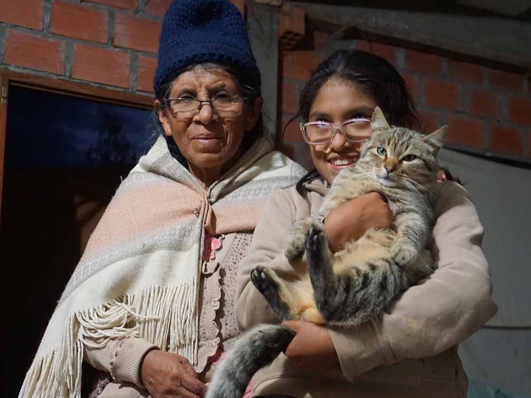 Ein Mädchen aus Bolivien hält eine Katze im Arm, die Mutter des Mädchens steht neben ihr.