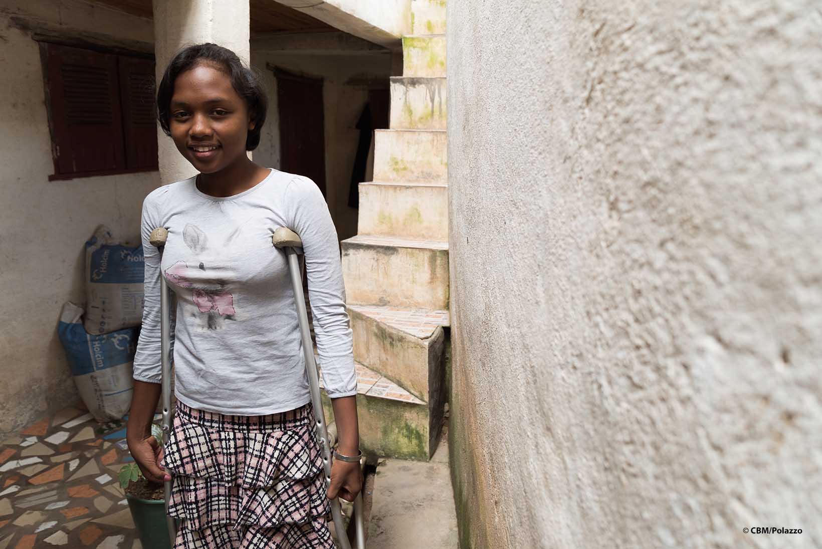 Eine Jugendliche mit körperlicher Behinderung aus Madagaskar an Krücken steht an einer Hauswand.