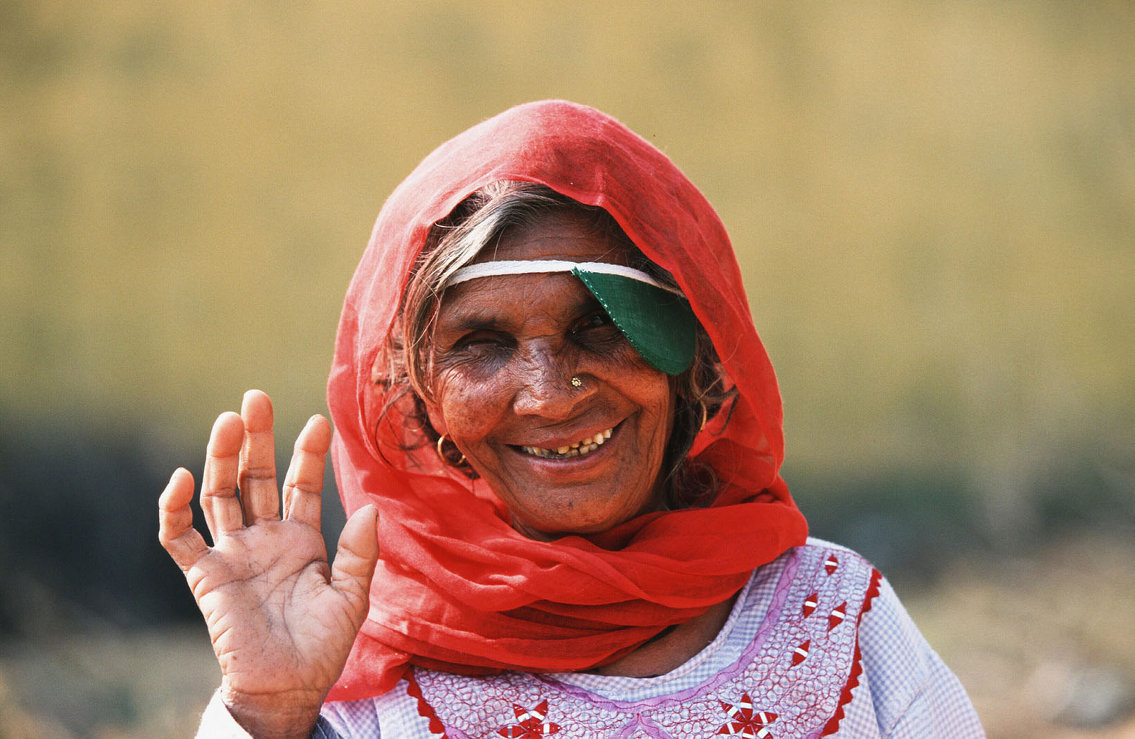 Un’anziana signora indiana con la benda sull’occhio sorride e saluta.