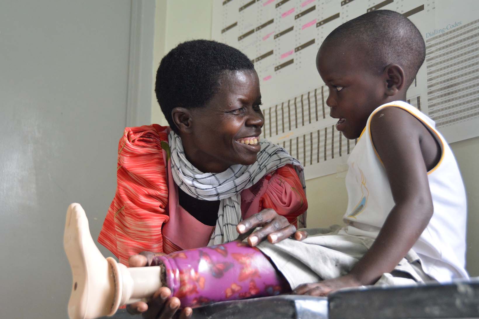 Una bambina dell’Uganda, con una protesi alla gamba, guarda la sua nonna sorridente.