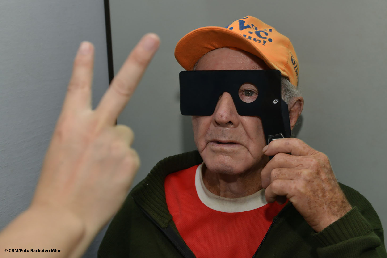 Ein Mann aus Bolivien hält sich eine Sichtabdeckung vor das Gesicht, sodass er nur mit dem linken Augen sieht, und versucht, die zwei Finger einer anderen Person zu erkennen.