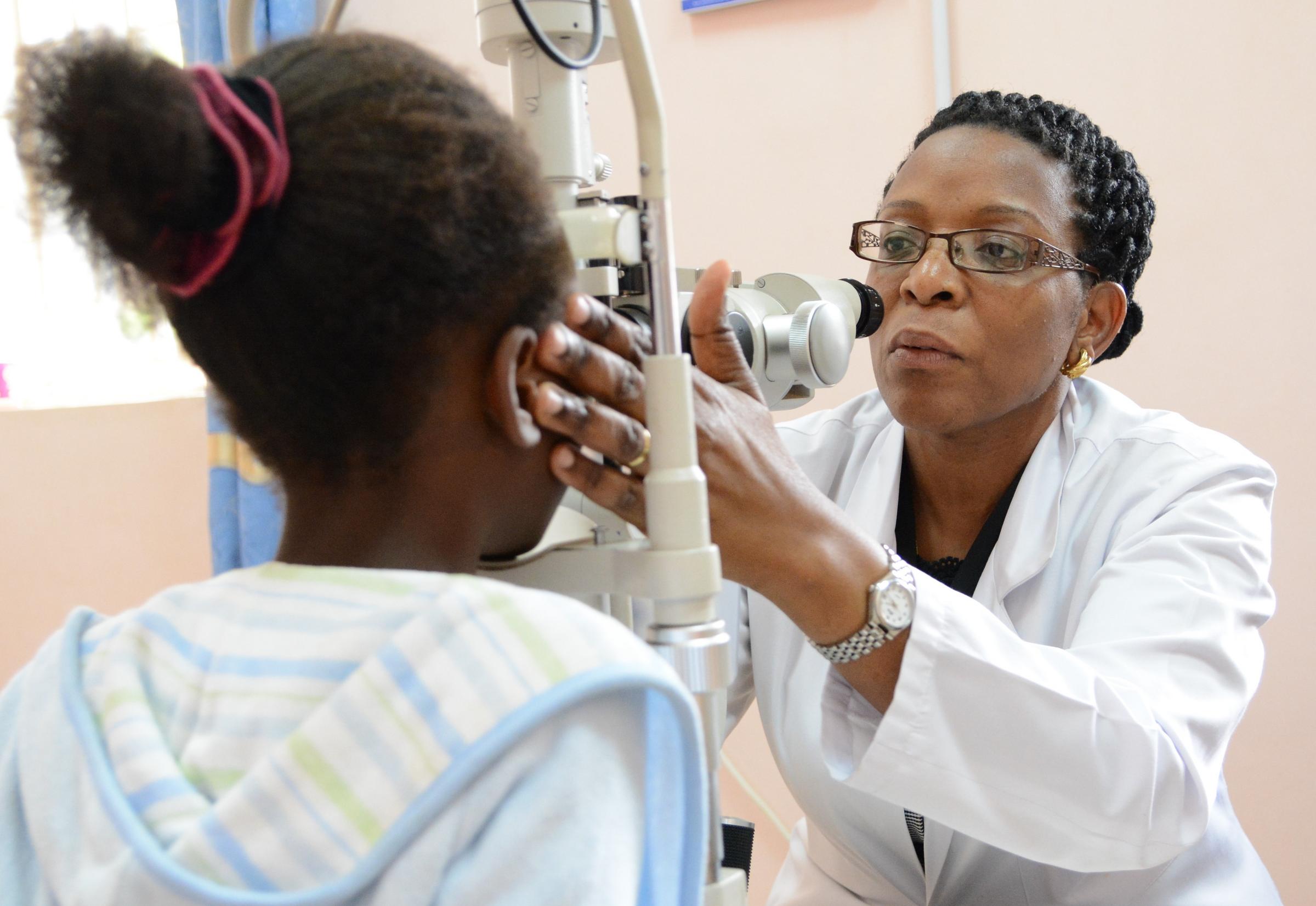 Eine Augenärztin und ein Mädchen aus Uganda sitzen sich gegenüber, dazwischen das Untersuchungsgerät, ein Spaltlampenmikroskop. 