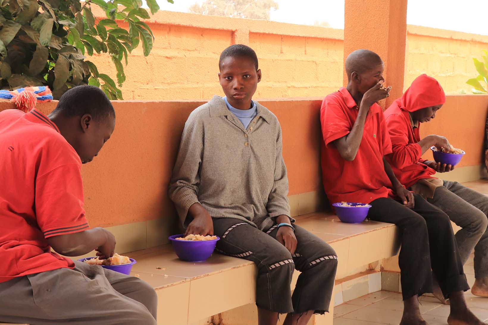 Mehrere Menschen aus Burkina Faso, die vorübergehend in einem Zentrum wohnen, essen aus einer Reis aus einer Schale.