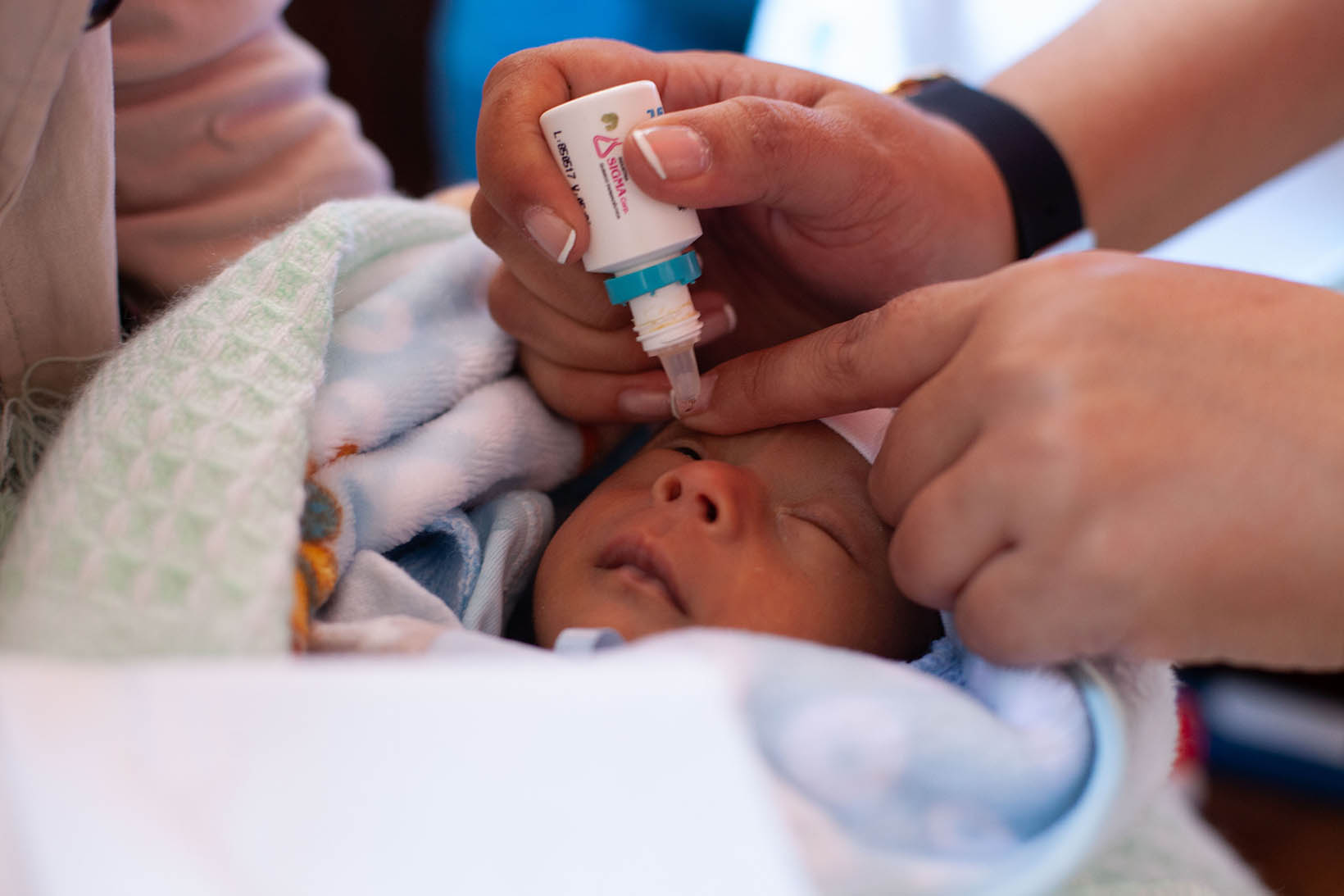 Eine Person aus Bolivien verabreicht einem Baby Augentropfen.