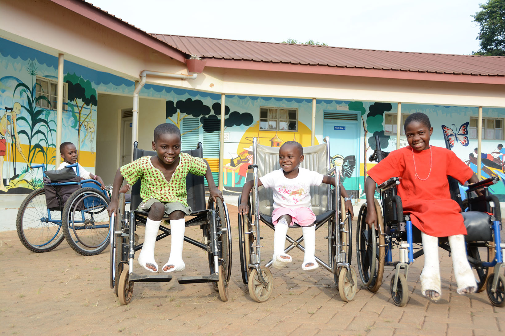 Due bambini e una bambina con le gambe ingessate siedono su una sedia a rotelle. 