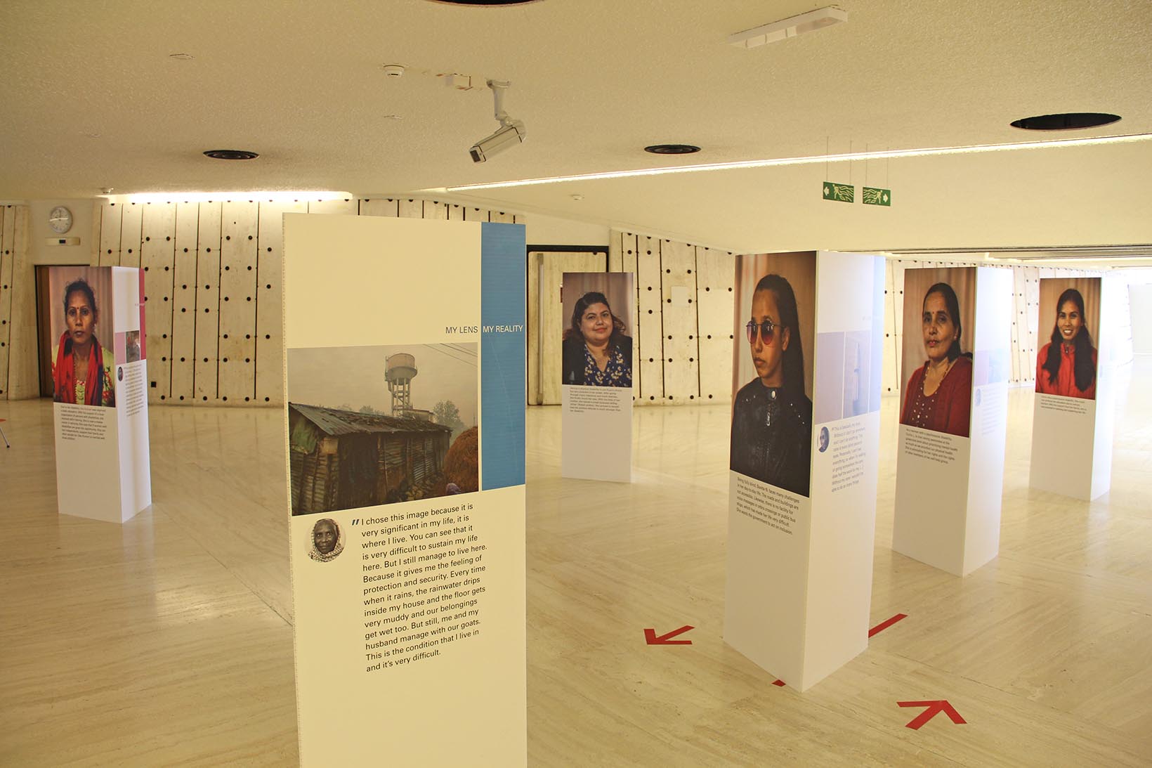 Eine Fotoaustellung in einem Gebäude der UNO in Genf. Es sind einige dreiseitige Panels zu sehen mit Porträtfotos von nepalesischen Frauen, mit weiteren Fotos aus ihrem Alltag sowie mit Zitaten von ihnen.