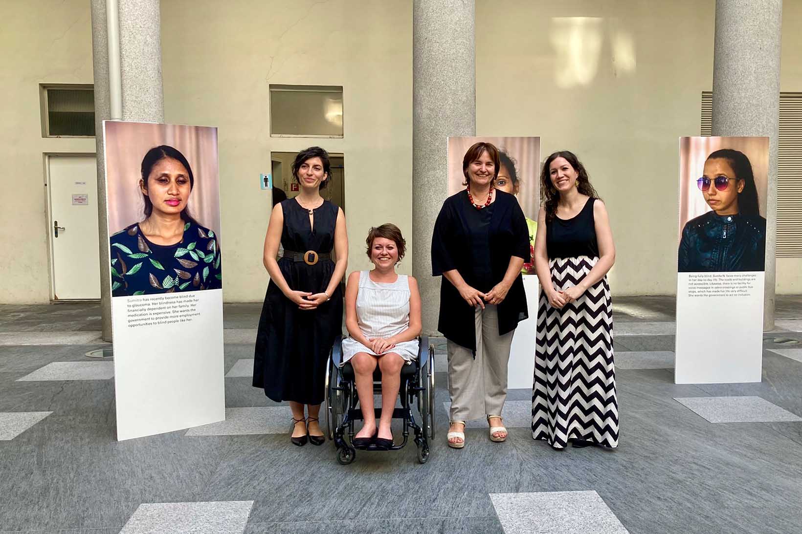Vier Frauen werden im Rahmen einer Fotoausstellung von vorne abgelichtet. Links und rechts von ihnen steht jeweils ein Fotoporträt einer nepalesischen Frau mit Behinderung.