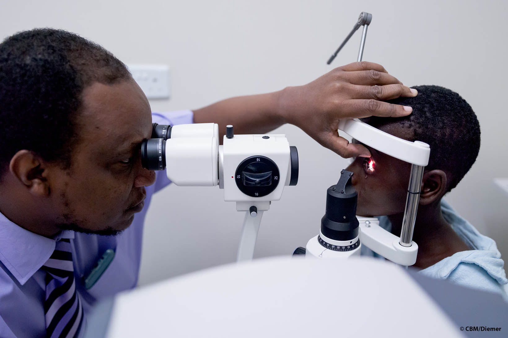 Un ophtalmologue du Zimbabwe ausculte l’œil d’une fillette au moyen d’une lampe à fraction.