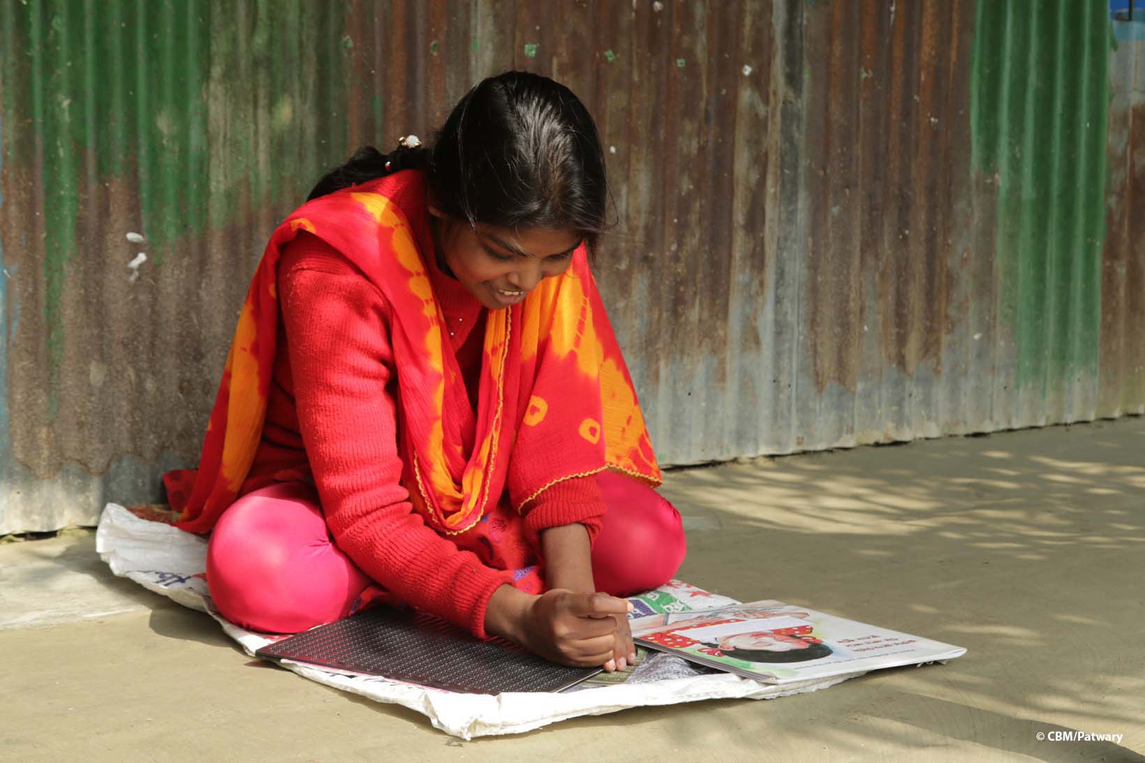 Eine blinde Frau aus Bangladesch sitzt auf dem Boden und schreibt in Braille.