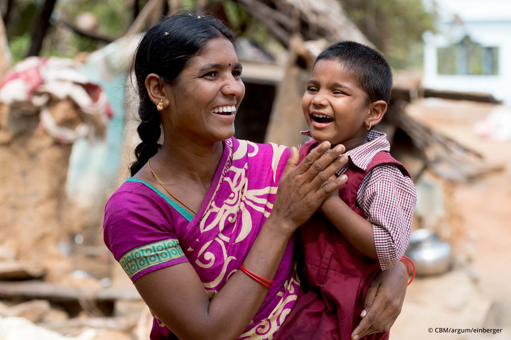 Eine Frau aus Indien hält ihre Tochter in Armen, beide lachen herzlich.