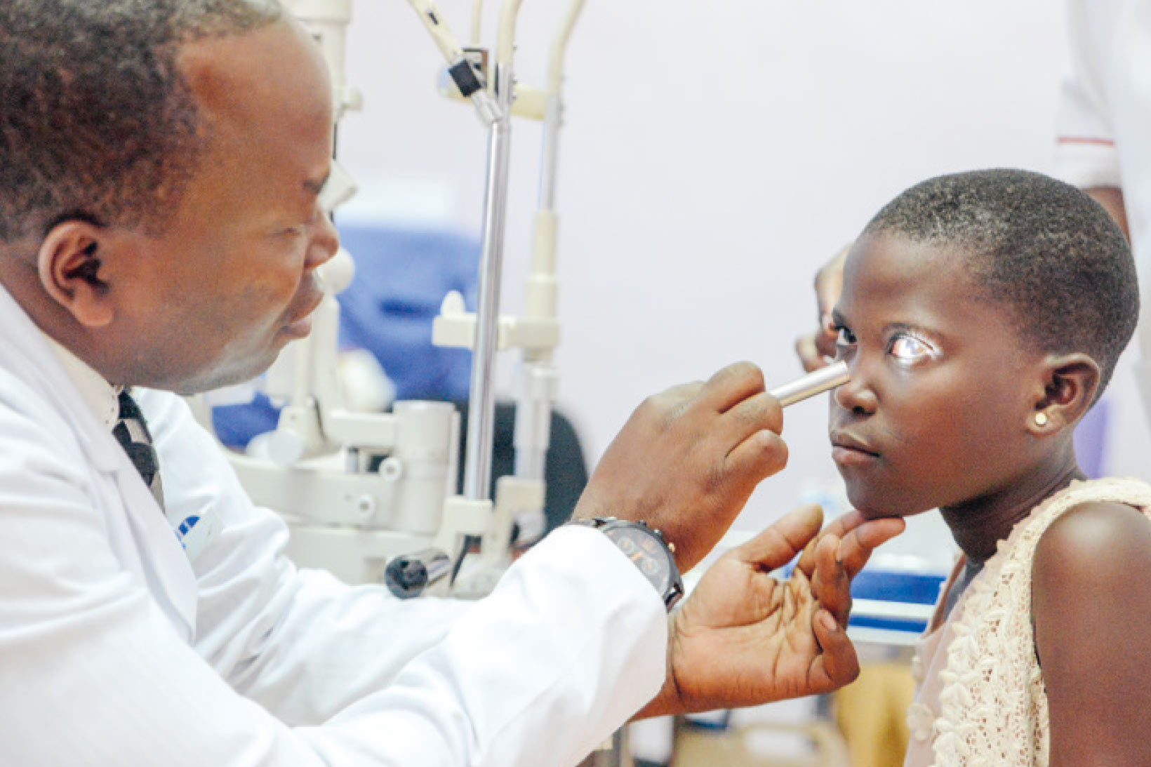 Ein Augenarzt aus Uganda leuchtet mit einer Taschenlampe in das Auge eines Mädchens.