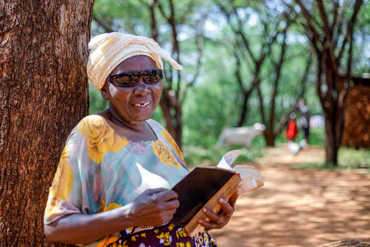 Francis Dora nach der Augenoperation unter einem schattigen Baum. Sie liest ein Buch. 