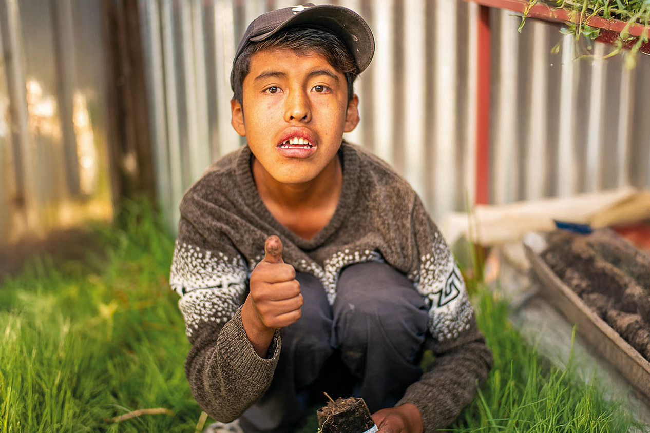 Dylan Mamani im Gewächshaus seiner Mutter. Der autistische Jung schaut in die Kamara und hält einen Daumen in die Höhe. 