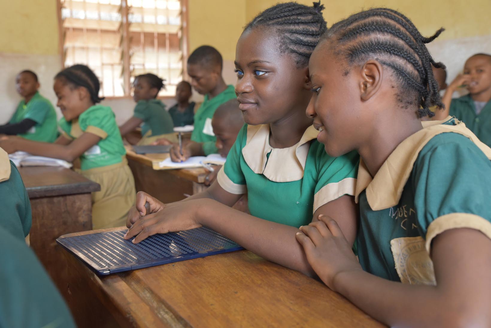 Une petite Camerounaise aveugle écrit des fiches en braille dans une classe d’école. Une fillette, assise à côté d’elle, la regarde faire.
