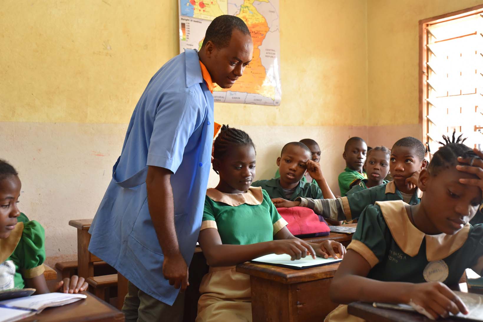 Un enseignant d’une école inclusive au Cameroun vérifie pendant la leçon les fiches en braille d’une élève aveugle.