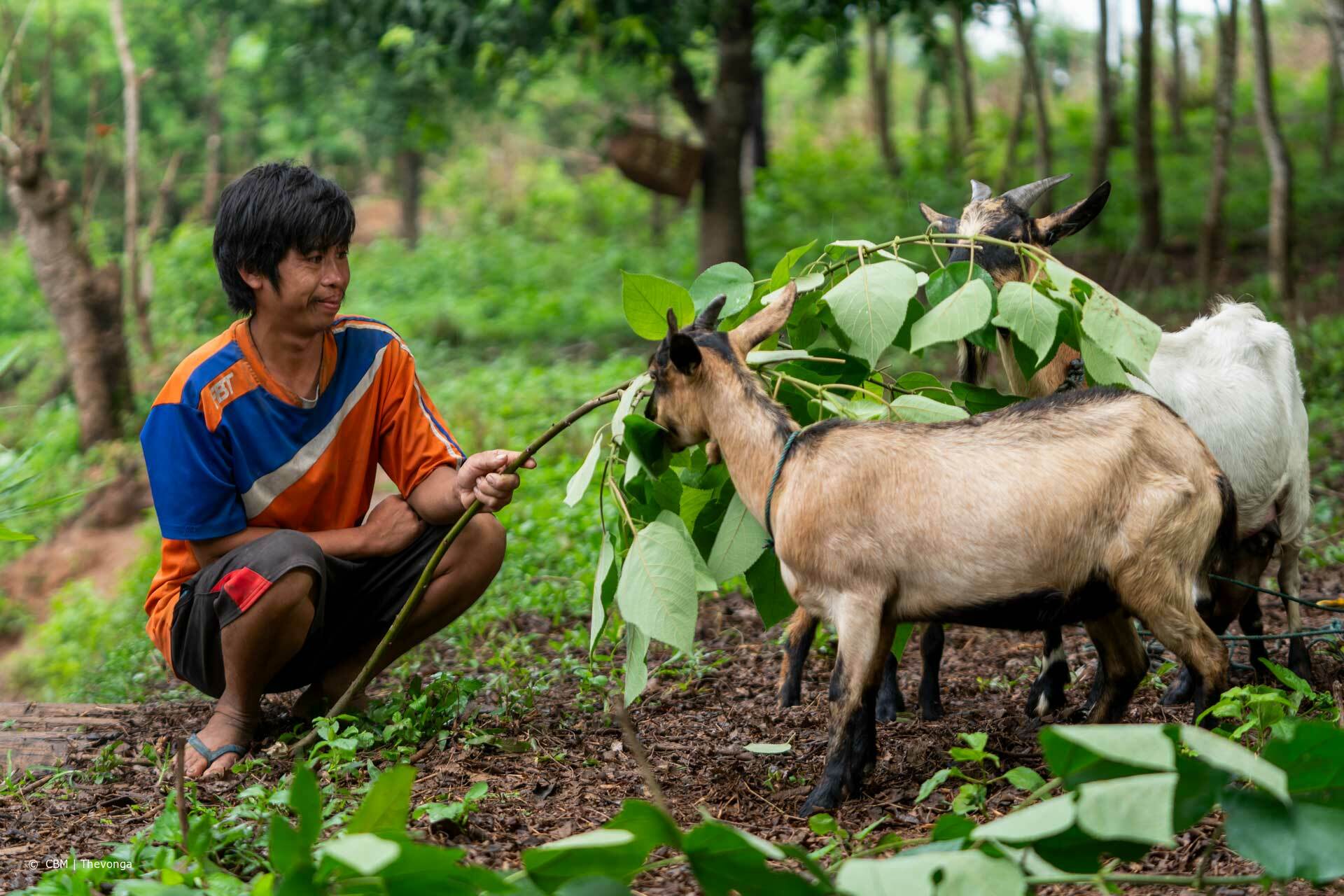 Auf dem Bild sieht man Khammai wie er zwei Ziegen füttert. 