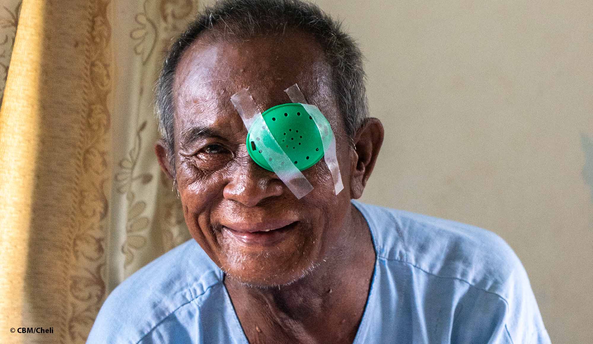 Porträt eines lächelnden Mannes aus Laos, der nach der Grauen-Star-Operation einen Augenverband über dem linken Auge trägt.