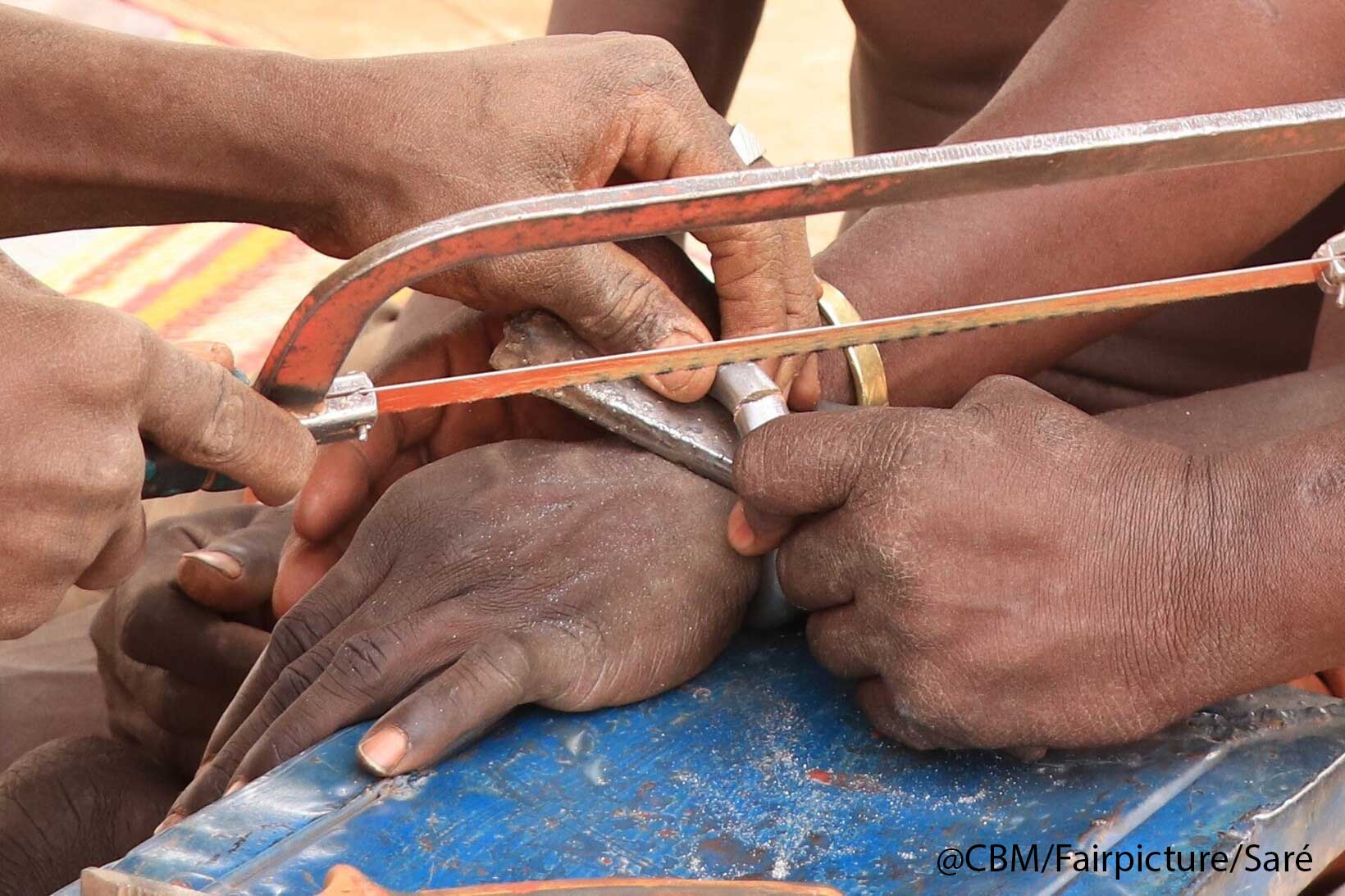 Das Bild zeigt Hände. Ousoeni Kindo wird mit einer Metalfile von seinen Ketten am Handgelenkt befreit. 
