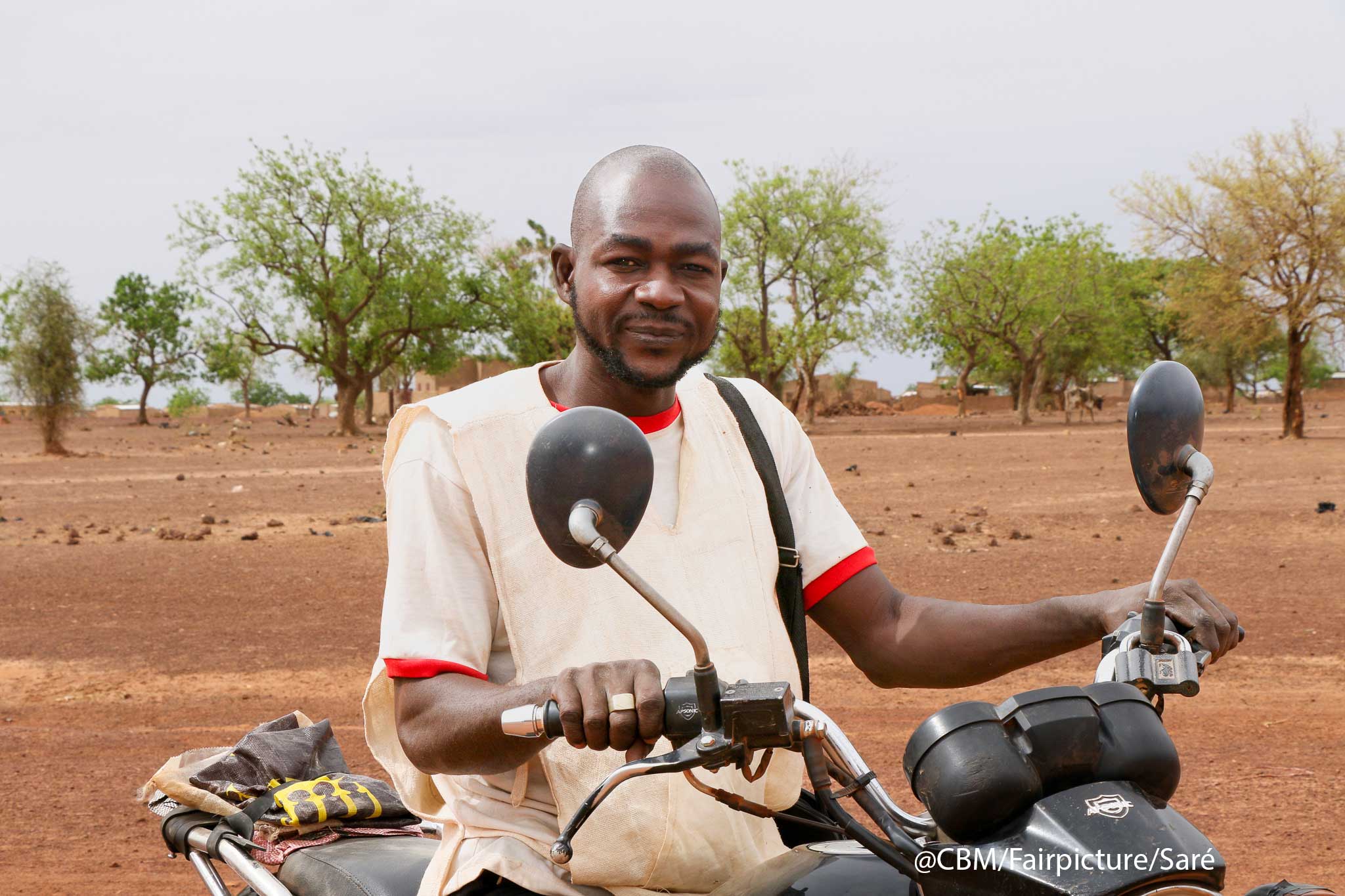 Ousoeni Kindo sitzt auf einem Motorrad und schaut zufrieden in die Kamera. 