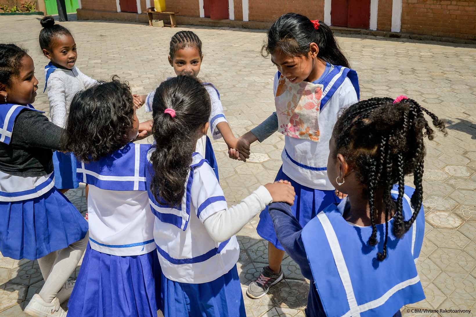 Schulkinder aus Madagaskar halten sich an den Händen und bilden einen Kreis. Eines der Kinder lebt mit einer körperlichen und kognitiven Behinderung.