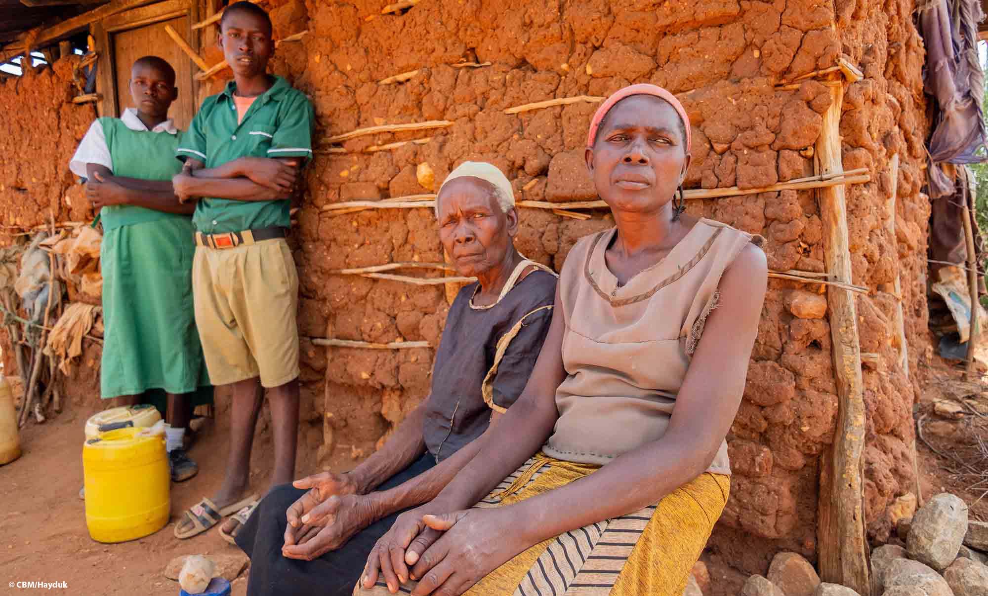Une famille kenyane est assise devant sa maisonnette en argile.