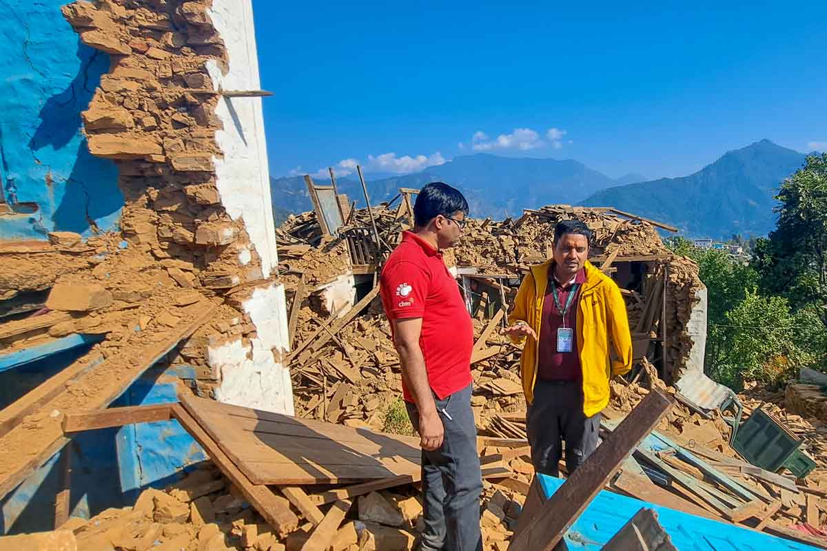 Die Koordinatoren stehen auf einem Trümmerhaufen bei einem komplett zerstörten Gemäude. 