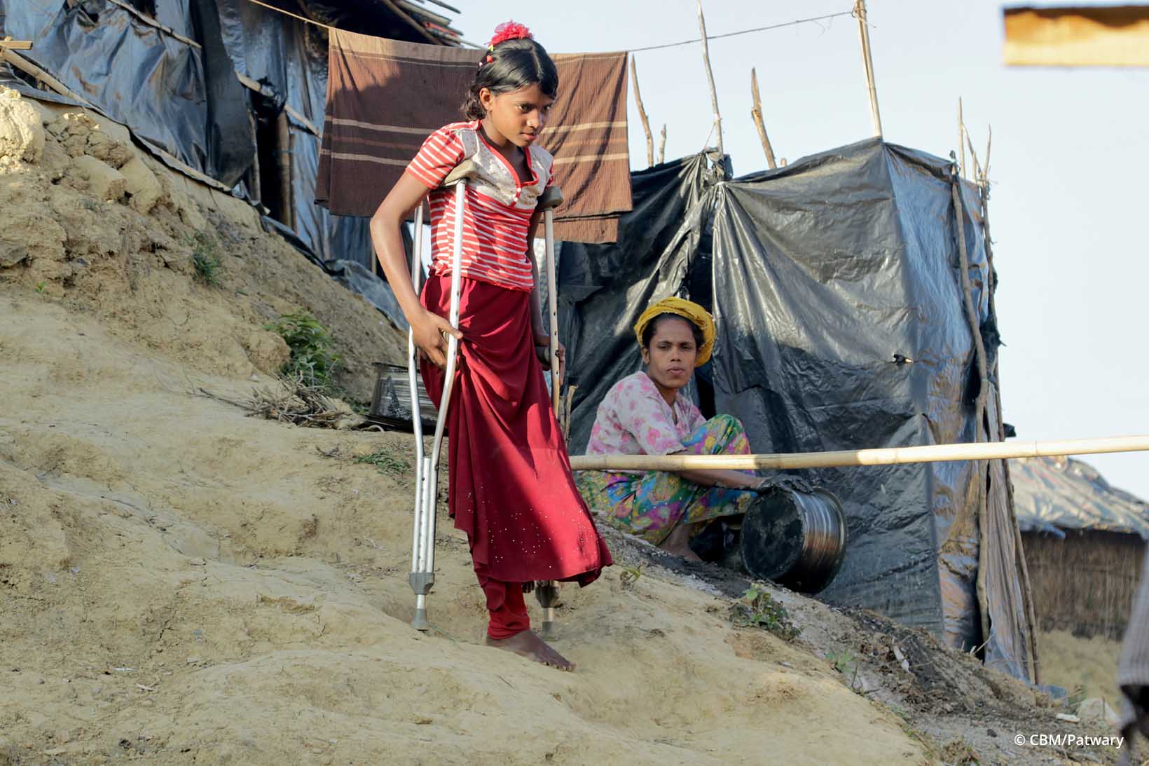 Une jeune fille Rohingya descend prudemment avec l’aide de béquilles un escalier construit dans la terre argileuse.