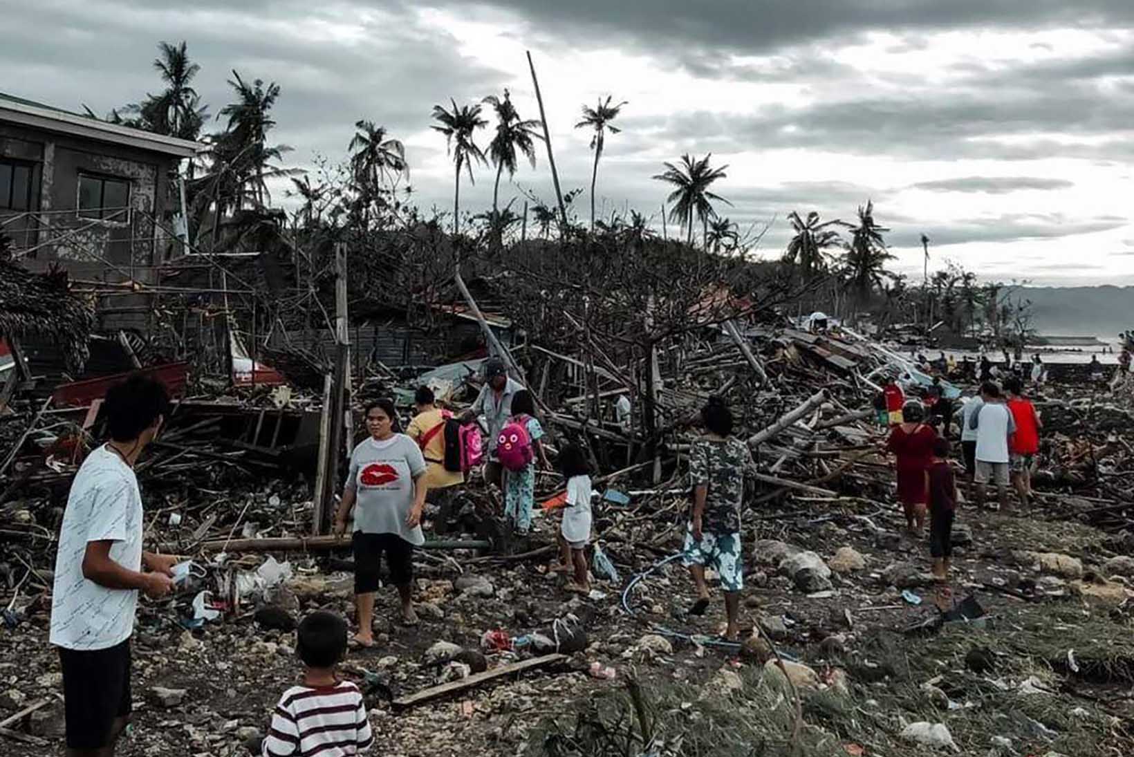 Personen aus den Philippinen stehen in den Trümmern eines Hauses.