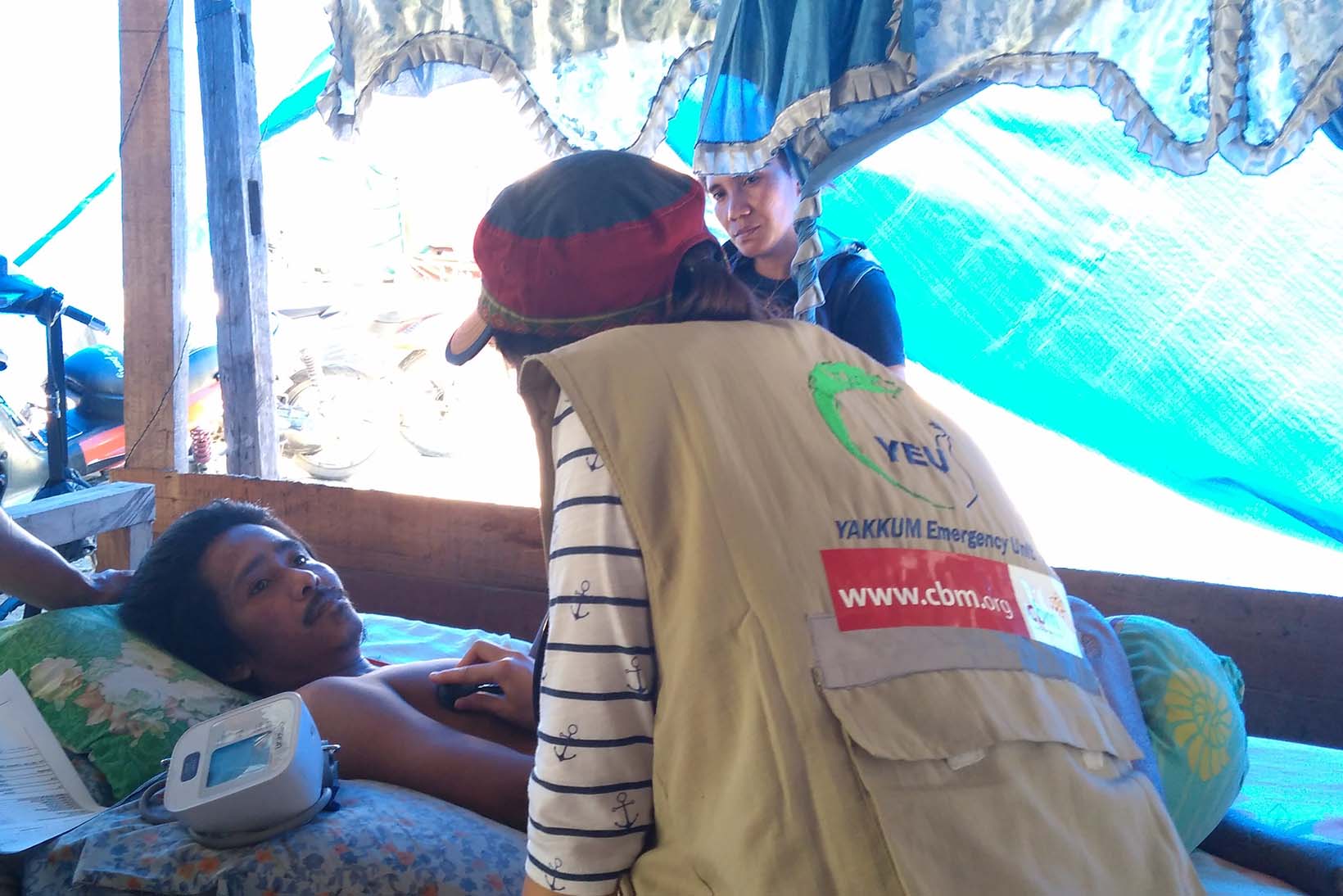 Ein auf dem Rücken liegender Mann aus Indonesien wird in einem mobilen Gesundheitsposten von einer Ärztin untersucht.