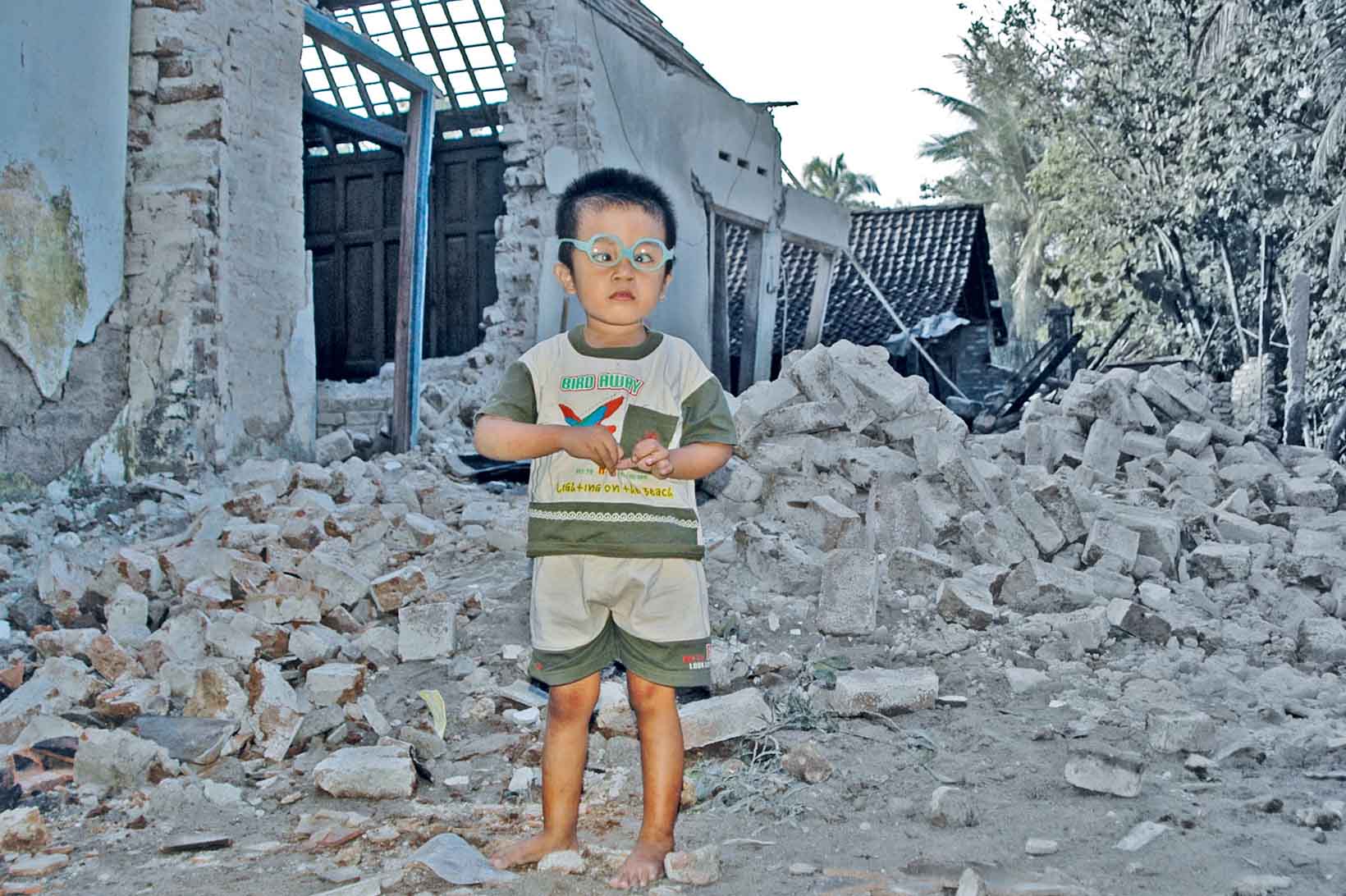 Un bambino in mezzo alle rovine di una casa crollata.
