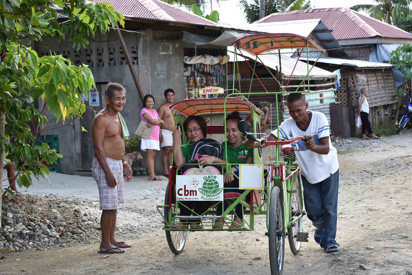 Ein Mann mittleren Alters aus den Philippinen, der mit Schizophrenie lebt, stösst sein Velotaxi. Darin sitzen zwei Frauen. 