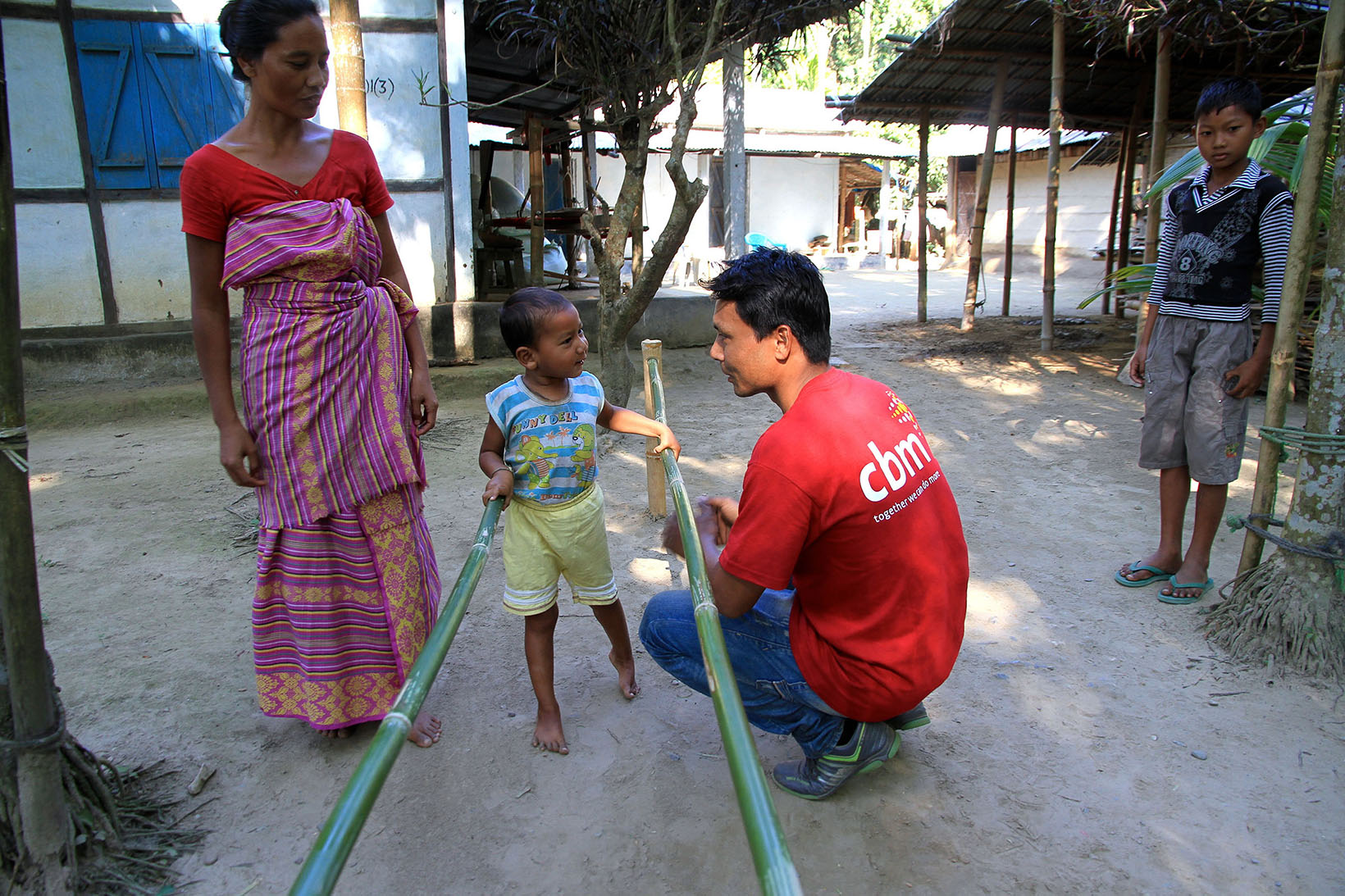 Un bambino indiano, appoggiato a barre parallele per la riabilitazione, parla con un uomo. 